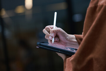 Close-up Asian man hand holding smartphone and using smart pen technology for writing on a tablet.
