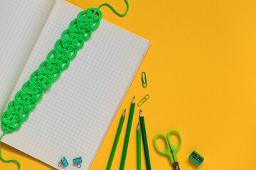 School stationery with green crochet bookmark on a yellow background. Top view. Copy space.