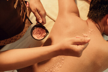 Masseuse hands holding salt scrub bowl for scrubbing on back customer at spa centre. Relaxation man customer get service skincare scrubbing massage with masseuse in spa salon. Selective focus.