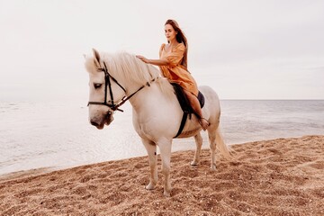 A woman in a dress stands next to a white horse on a beach, with the blue sky and sea in the background.