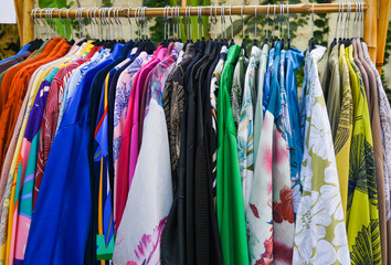 Rack with stylish women's colorful printed bright clothes near at street market.