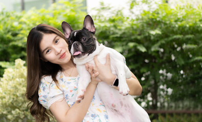 Portrait of happy young Asian girl in good mood standing and holding her lovely French bulldog with pleasure