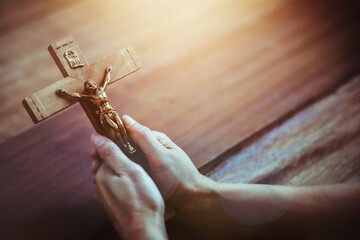 Close up of human hand holding the crucifix of Jesus Christ with the sun light on wooden table Christian believe , trust or easter concept
