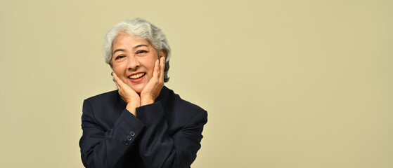 Smiling senior businesswoman wearing black suit and eyeglasses standing isolated on beige background