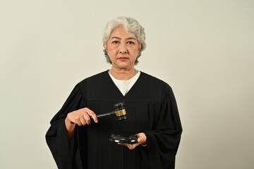 Senior female judge in robe gown uniform holding a gavel in hand and looking confidently to camera. Lawyer, justice and law, attorney
