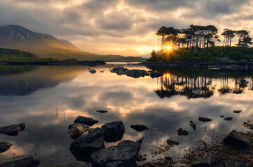 Dramatic cloudy sunrise lakeside landscape scenery of twelve pines island reflected in water surrounded by mountains at Derryclare, connemara national Park in County Galway, Ireland 