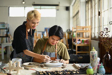 Young potter helping student shaping and scraping raw Clay in the bright ceramic workshop