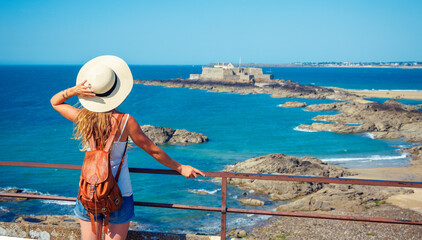 Young woman looking at atlantic ocean coast and fort- Saint Malo in France, travel destination, tour tourism,vacation concept - obrazy, fototapety, plakaty