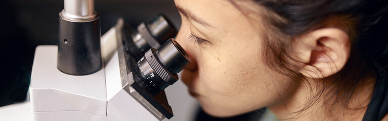 Asian lady doctor looks into contemporary microscope researching sample on slide in hospital