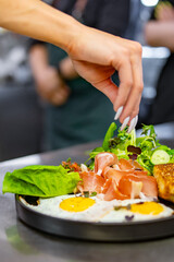 woman chef hand cooking fried eggs with ham, salad and hummus