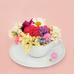 Surreal summer flowers and wildflowers teacup composition on pink background with scattered flowers. Abstract fun health food floral medicinal nature surrealism design.

