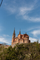 Vertical view of the basilica of Santa María la Real de Covadonga in the tourist province of Asturias on a hill with its medieval architecture in a reddish tone with the blue sky at the back