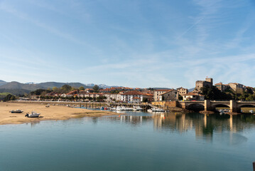 Fototapeta na wymiar Panoramic view of the tourist village of San Vicente de la Barquera with an impressive stone bridge. Low tide, colourful fishing boats and small houses on a sunny day in Cantabria.