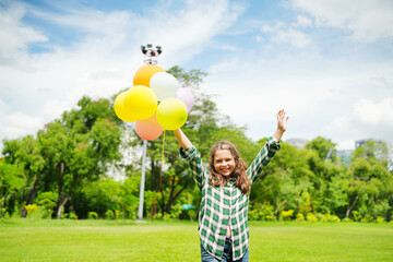 Cheerful cute girl holding balloons running on green meadow white cloud and blue sky with...