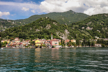 Fototapeta na wymiar Lake Como with Varenna Town on Shore and Rocky Green Hills in Italy. Picturesque View of European Village and Nature during Summer Travel.