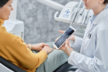 Closeup of female dentist showing x ray images on tablet to female patient in clinic, copy space