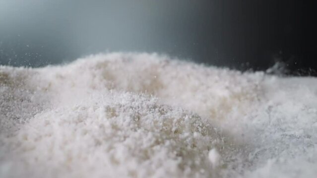 Coke powder bounces on concave surface against dark grey wall. White substance with psychoactive properties sifting through sieve moves lying on working panel macro