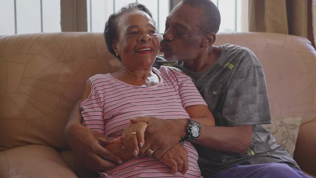 A black Brazilian adult son and elderly mother embrace seated on couch smiling at camera. African American family relatives people portrait