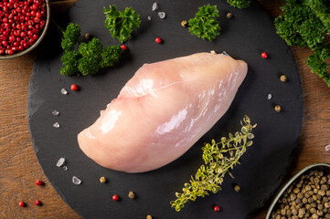 Raw chicken breast. Raw chicken breast fillet with spices and herbs on slate board. Wooden Background.