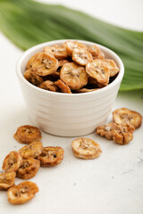 Dried fresh organic banana slices in glass bowl with green leaf.Macro