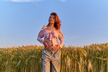 A pregnant woman is holding her stomach in the middle of a wheat field. A girl is expecting a baby at sunset in summer. Fatherhood and motherhood among young people