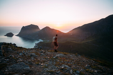 Young athletic man with backpack hike to reach summit of mountain at sunset. Cinematic beautiful adventure. Inspiring time spent outdoors. Explore norway in summer