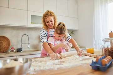 Mother and daughter kneading cookie dough with rolling pin at home