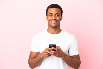 African American handsome man on isolated pink background looking at the camera and smiling while using the mobile