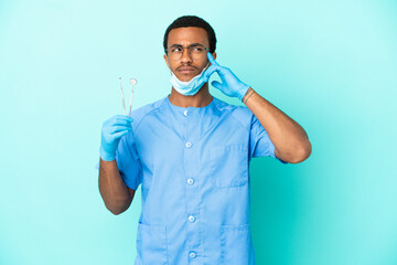African American dentist holding tools over isolated blue background having doubts and thinking