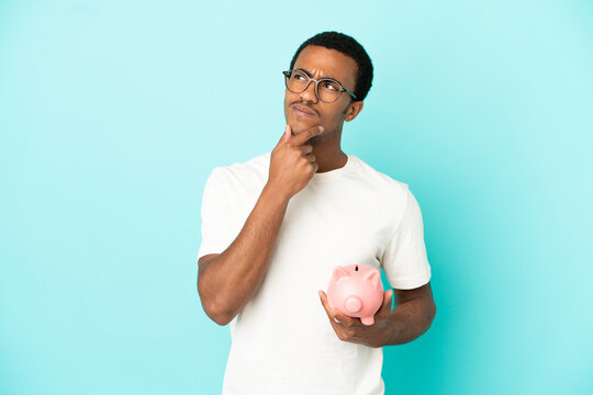 African American handsome man holding a piggybank over isolated blue background having doubts