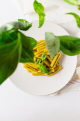 Top vertical view of pasta with pesto dish, with flying basil leaves, white napkin and white background