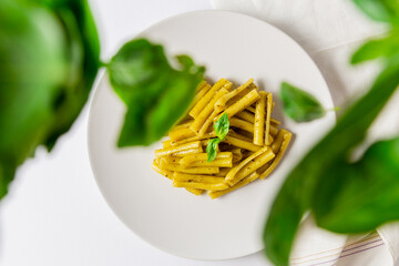 Top view of pasta with pesto dish, with flying basil leaves, white napkin and white background