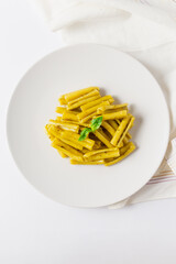 Top vertical view of pasta with pesto dish, with basil leaves, white napkin and white background