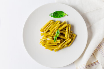 Top view of pasta with pesto dish, with basil leaves, white napkin and white background