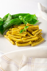 Front vertical view of pasta with pesto dish, with basil leaves, white napkin and white background