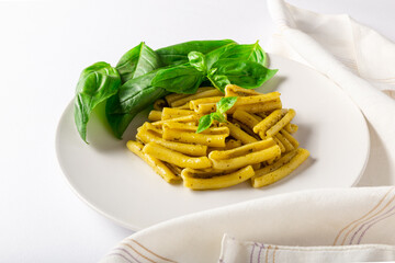 Front view of pasta with pesto dish, with basil leaves, white napkin and white background