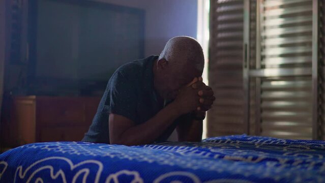 African American senior Praying at home by bedside. A religious black older person on his knees in Prayer. Spiritual concept of HOPE and FAITH