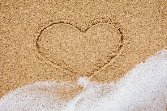 A drawing of a heart on wet beach sand at a beautiful seascape.Texture.Sea waves on sand
