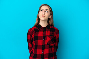 Fototapeta premium Young caucasian woman isolated on blue background and looking up