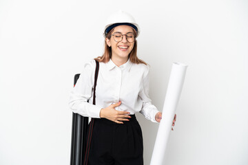 Young architect woman with helmet and holding blueprints isolated on white background smiling a lot