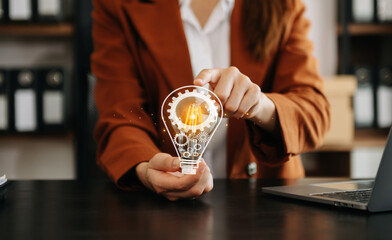 Hand of a woman with a light bulb And there is a gear icon in it And he is using a laptop and tablet. The idea of ​​inspiration from online technology.