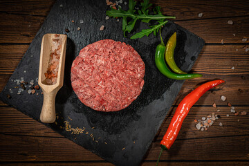 Raw beef hamburger patties with herbs and spices on dark wooden plate