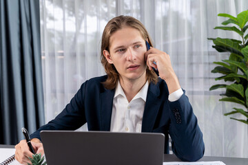 Hardworking and diligent businessman working on his laptop while talking to clients on his mobile...