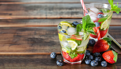 Cold mojitos with strawberries and blueberries. Glasses of mojito and fruits on a wooden background. Summer cocktails. Copy space.