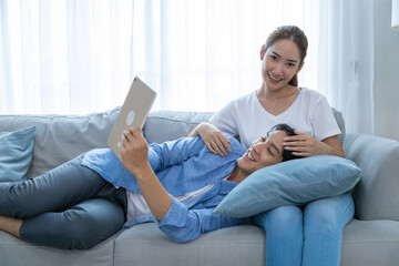 Young couple watching tv series laughing happily using tablet and sitting on sofa bed