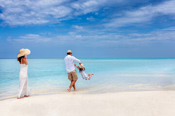 A happy family has fun in the turquoise ocean of a tropical paradise beach in the Maldives during...