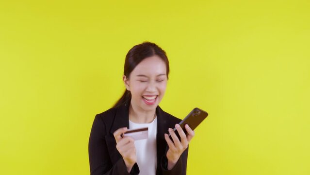Portrait young asian business woman hold credit card and looking smart phone for shopping online isolated yellow background, businesswoman looking debit card and smartphone, financial concept.