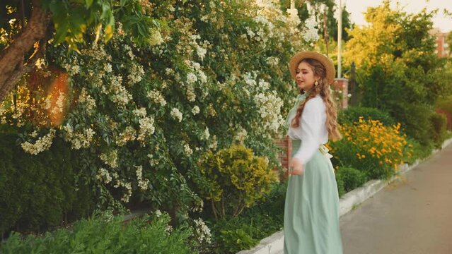 Cheerful happy joyful young woman red long loose hair fly wind throws. cute Girl spinning dancing hands raised to magic sun light flare sunset. Beauty Smiling face. summer nature reen trees. boat hat 