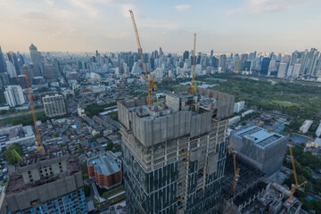 Fototapeta premium Aerial view of a large construction of a residential area with many multi-storey buildings under construction, a lot of tower cranes, workers, construction equipment at sunset 