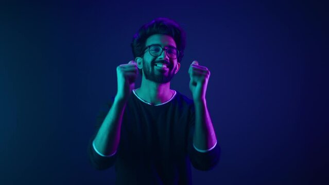 Portrait in neon ultraviolet happy Indian guy Arabian man worker coder hacker computer engineer make gesture hey you showing index finger front direction at camera thumbs up agree support recommend